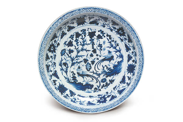 元代．青花雉鸡竹石花果纹盘，此器以雉鸡竹石花果为主纹，搭配斜格锦纹和带状莲花，做同心圆式的布局。（图三）+图片来源：《幽蓝神彩》，页107，图24。